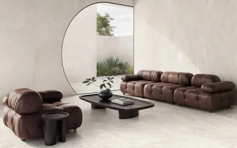 Salotto moderno con divano e poltrona in pelle marrone, tavolino in legno scuro e vista su un giardino interno. L'ambiente evoca la serenità di una casa provenzale.