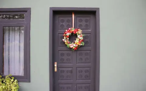 Ghirlanda natalizia appesa con un nastro alla porta scura, un esempio di come appendere la ghirlanda alla porta per le feste.