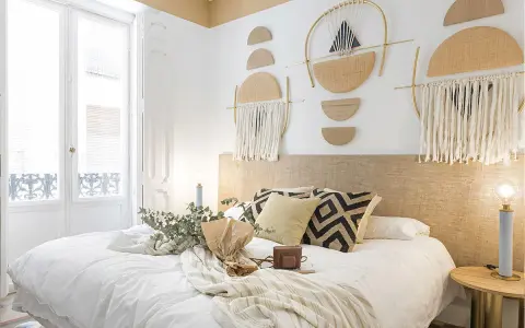 Accogliente camera da letto stile boho con decorazioni murali geometriche, tessuti naturali e un letto invitante.
