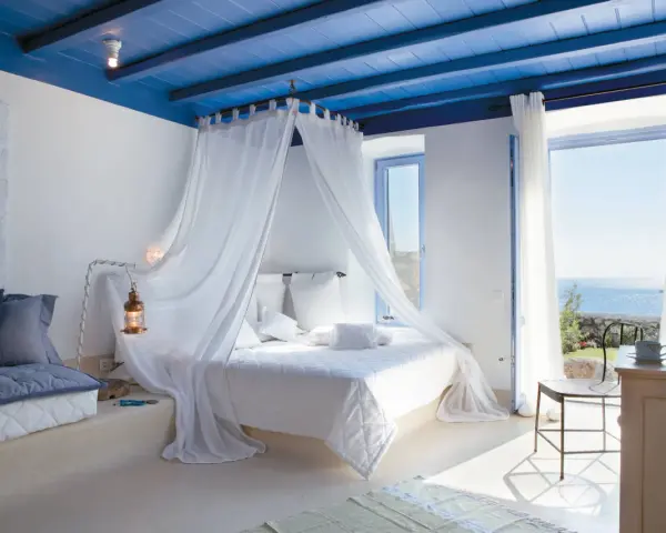 Camera da letto stile mediterraneo con soffitto blu, letto a baldacchino bianco e vista mare.