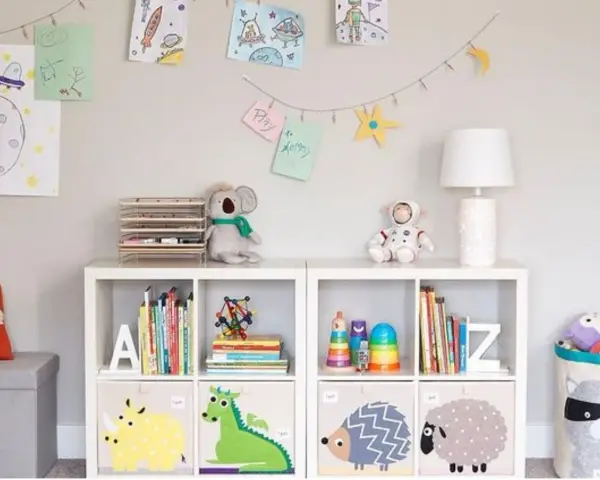 Soluzione creativa per come sistemare i giochi in salotto: scaffali bianchi con contenitori decorati e libri ordinati.