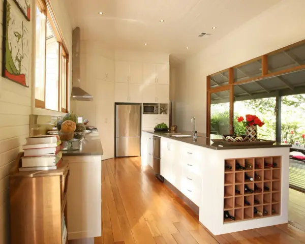 Cucina moderna con isola centrale dotata di una cantina a vista per il vino. Ampie vetrate si aprono su un patio esterno.