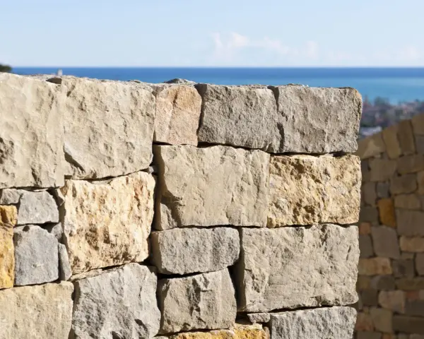 Muro a secco per contenimento terra, con vista sul mare e un borgo in lontananza.