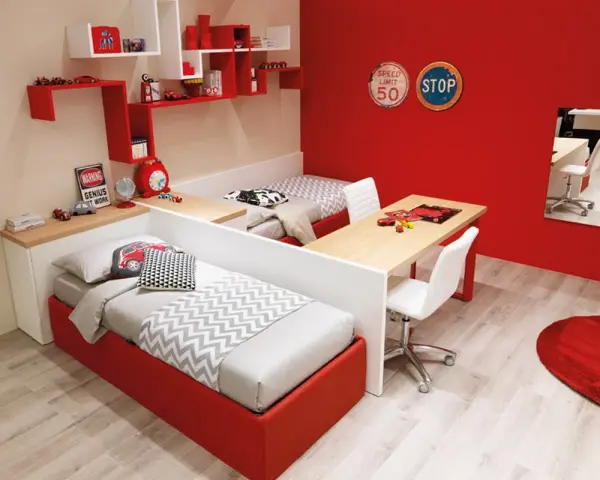 Una parete divisoria crea due spazi separati in una cameretta, con letti rossi e scrivanie.