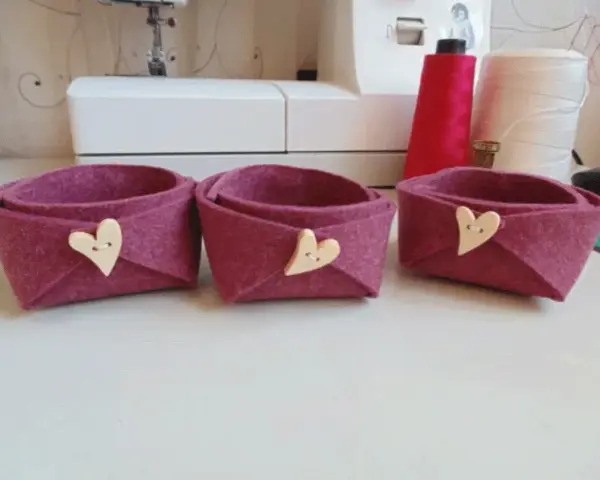 Tre cestini in feltro fai da te, color melanzana, decorati con bottoni a forma di cuore. Perfetti per organizzare piccoli oggetti.