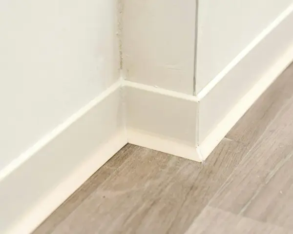 Angolo di una stanza con parquet grigio e battiscopa bianco appena installato.