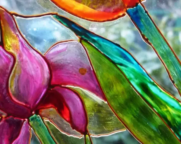 Dettaglio di un fiore dipinto su vetro, con petali viola e verdi vibranti. Un'ispirazione per il **dipinto su vetro fai da te**.