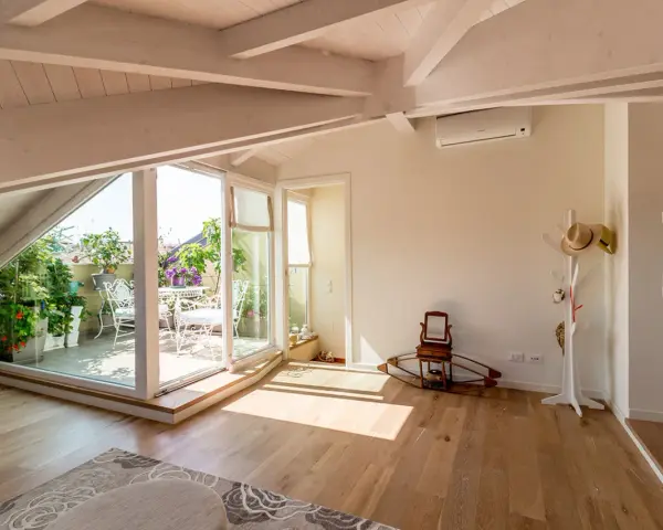 Luminoso sottotetto con travi a vista e un terrazzo fiorito. Idee sottotetto molto basso per sfruttare ogni angolo.