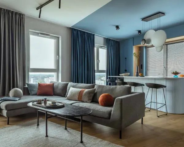 Soggiorno moderno con divano grigio, tavolino nero e tende blu e grigie. Un esempio di come scegliere le tende per il salotto per un look sofisticato.