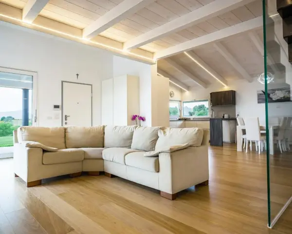 Soggiorno moderno con travi in legno sbiancate senza carteggiare, divano beige e cucina a vista.
