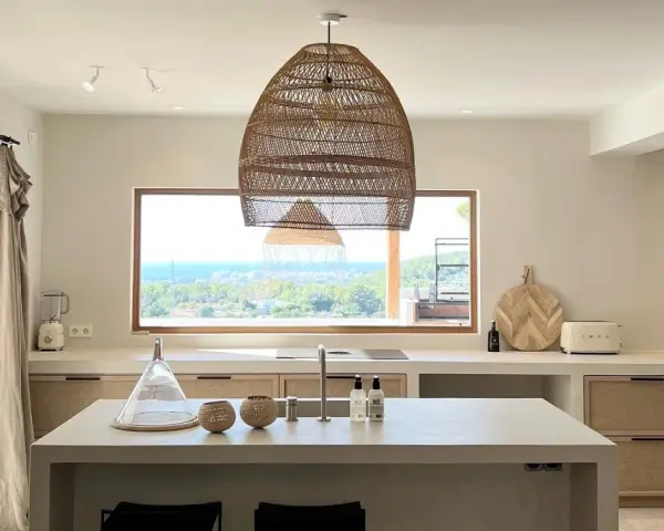 Cucina luminosa con isola centrale, lampadario in rattan e vista mare. Arredamento in stile casa bohemien con materiali naturali.