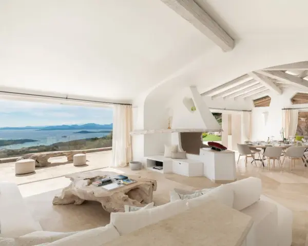 Soggiorno luminoso con vista mare, perfetto per l'arredo case al mare. Divani bianchi, camino moderno e tavolo da pranzo per godersi il panorama.