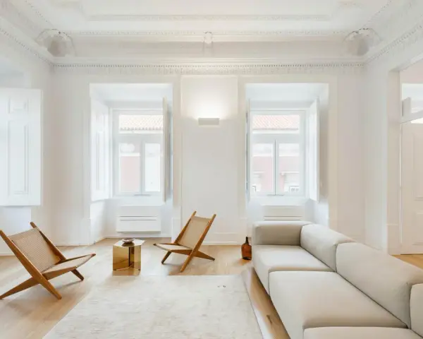 Soggiorno minimalista con divano chiaro, sedie in legno e tavolino dorato. Un esempio di come un consulente d'arredo può creare un ambiente luminoso e accogliente.