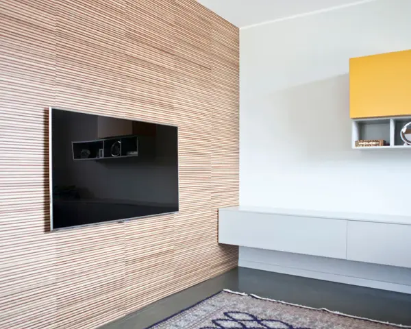 Pannellatura a righe per rivestire una parete interna in modo economico, con TV incassata e mensole moderne.