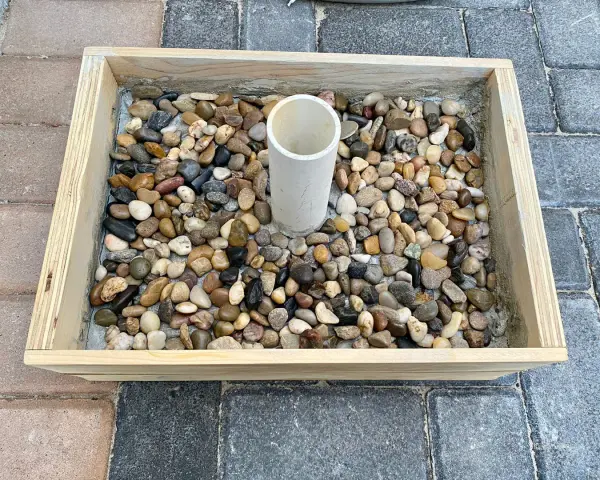 Base per ombrellone fai da te: un contenitore in legno riempito di ghiaia con un tubo centrale per l'asta.