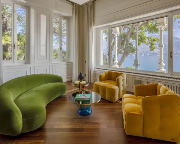 Un salotto con divano verde curvo e poltrone gialle, tavolini rotondi e vista lago. Un perfetto esempio di **art deco arredamento** con tocchi moderni.