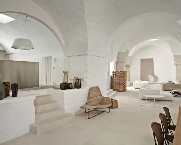 Interni moderni con soffitti a volta, un'elegante cucina a vista, zona living con divani e poltrone in vimini, e dettagli decorativi in ceramica.