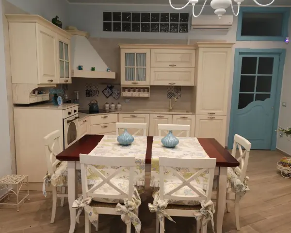 Accogliente piccola tavernetta casa con cucina in legno chiaro, tavolo da pranzo e porta azzurra.