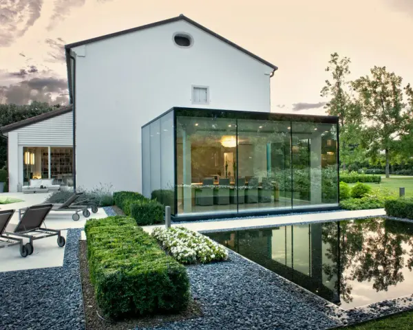 Ampliamento casa con estensione esterna in vetro, con piscina e arredi da giardino.