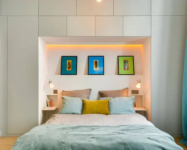 Idee salvaspazio camera da letto piccola: letto con testiera contenitore, quadri colorati e tende turchesi creano un ambiente accogliente.