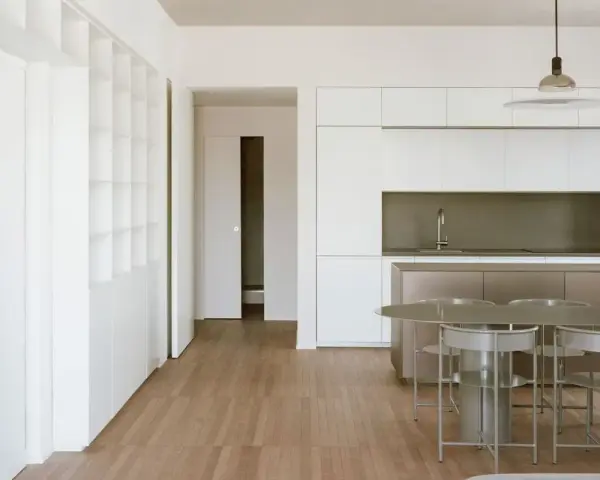 Interni moderni con cucina a isola, tavolo e sedie. Ampia libreria a muro, segno di un **cambio destinazione d'uso da magazzino ad abitazione**.