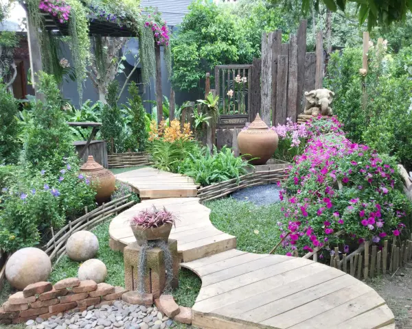 Percorso sinuoso in legno tra fiori vivaci e vasi in terracotta, con elementi decorativi che evocano idee giardino zen.