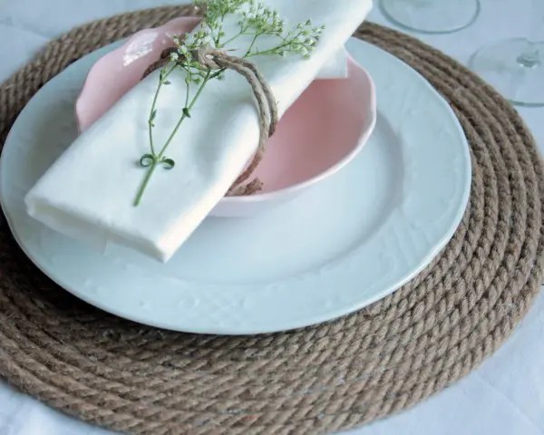 Sottopiatti in stoffa fai da te, con tovagliolo bianco legato da spago e decorato con un rametto fiorito.
