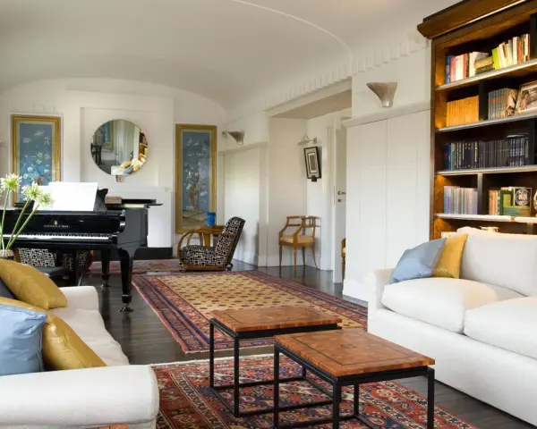Salotto con pianoforte a coda, divani bianchi, tappeti orientali e libreria. Un perfetto esempio di arredamento classico moderno.