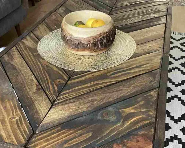 Tavolo con pallet fai da te, con un cesto di frutta in legno e un tappeto geometrico.