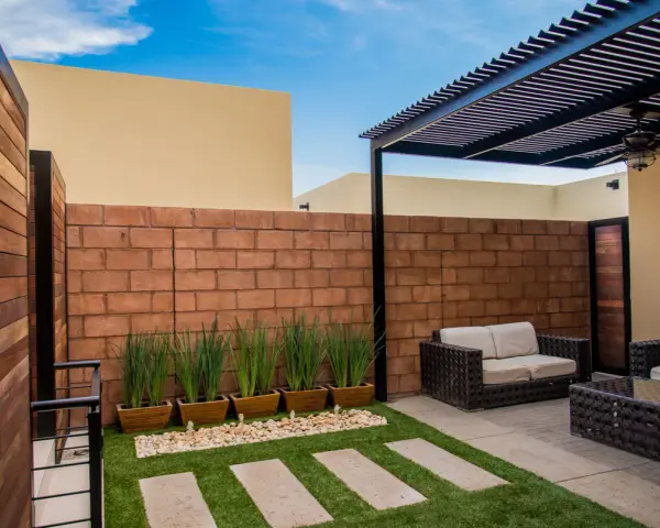 Un cortile in cemento trasformato con erba sintetica, piante in vaso e arredi da esterno. Idee per come abbellire un cortile in cemento.