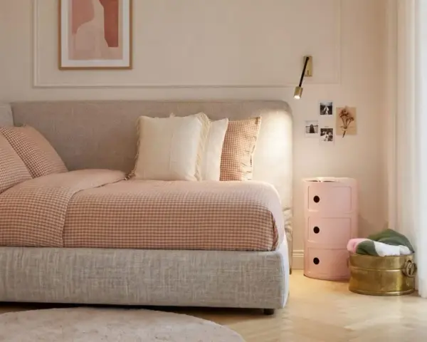 Un angolo letto con biancheria a quadri, cuscini morbidi e un quadro astratto. L'ambiente è accogliente, perfetto per creare camere aesthetic.