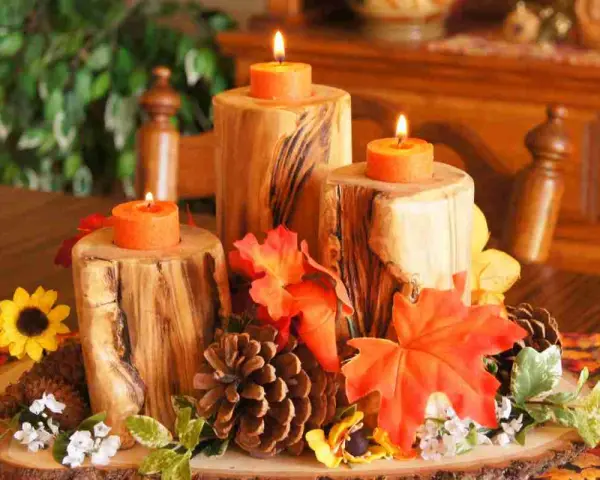Un semplice centrotavola autunnale con tronchi di legno, candele arancioni, pigne e foglie colorate.