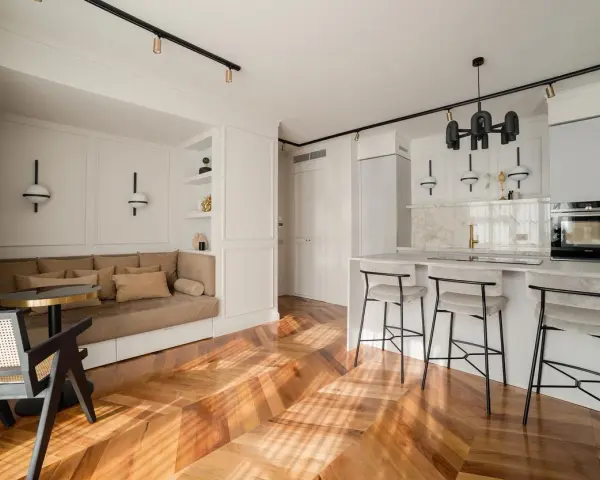Open space con ingresso aperto su soggiorno. Divano angolare, bancone cucina con sgabelli e parquet a spina di pesce.