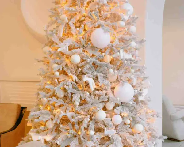 Albero di Natale innevato con luci calde, palline bianche e dorate, e decorazioni a forma di angeli e cervi. Un'elegante idea per un albero di Natale bianco e oro.