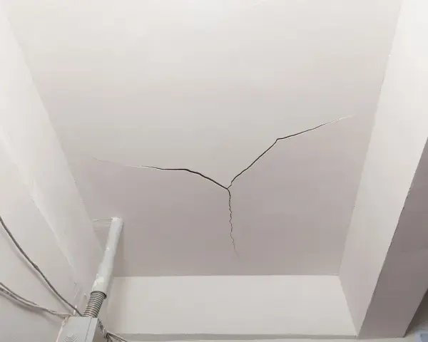 Crepe sul soffitto, un segno che il tempo o un problema strutturale sta lasciando il suo segno. Cavi elettrici e un tubo corrono lungo il muro.