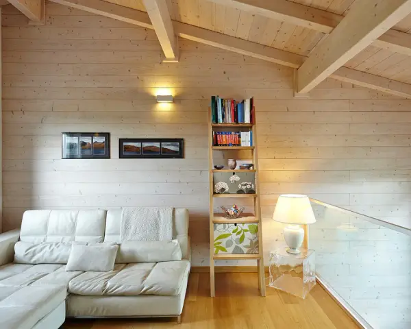 Soggiorno accogliente con divano bianco, libreria a giorno e un suggestivo tetto in legno a vista.