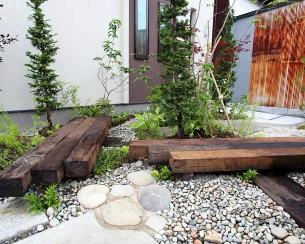 Un piccolo giardino zen con panchine in legno riciclato, ghiaia e piante verdi. Perfetto per idee giardino piccolo fai da te.