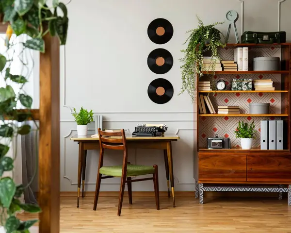 Scrivania con macchina da scrivere e sedia verde, libreria con dischi in vinile e piante. Perfette idee arredamento vintage per un angolo studio.