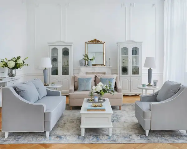 Salotto luminoso in stile shabby chic contemporaneo, con divani grigi, mobili bianchi e dettagli dorati.