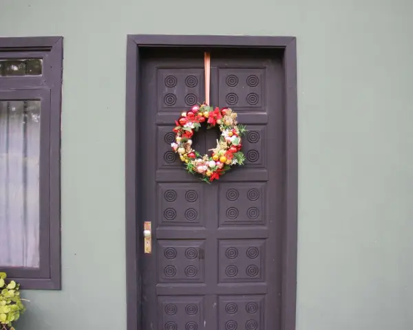 Ghirlanda natalizia appesa con un nastro alla porta scura, un esempio di come appendere la ghirlanda alla porta per le feste.