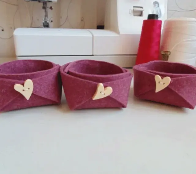 Tre cestini in feltro fai da te, color melanzana, decorati con bottoni a forma di cuore. Perfetti per organizzare piccoli oggetti.