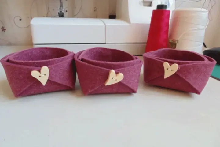 Tre cestini in feltro fai da te, color melanzana, decorati con bottoni a forma di cuore. Perfetti per organizzare piccoli oggetti.