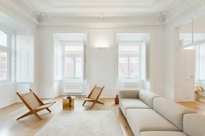 Soggiorno minimalista con divano chiaro, sedie in legno e tavolino dorato. Un esempio di come un consulente d'arredo può creare un ambiente luminoso e accogliente.