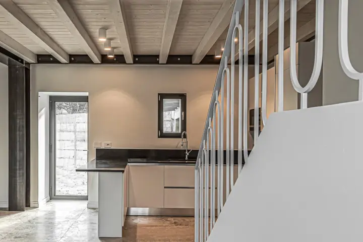 Interno moderno con travi a vista in legno, illuminazione led soffusa e una scala bianca.
