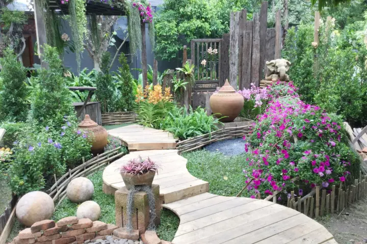 Percorso sinuoso in legno tra fiori vivaci e vasi in terracotta, con elementi decorativi che evocano idee giardino zen.