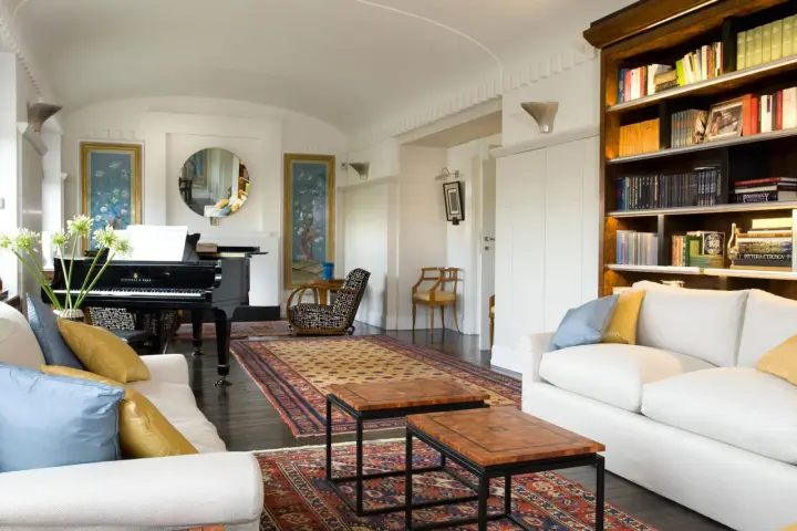 Salotto con pianoforte a coda, divani bianchi, tappeti orientali e libreria. Un perfetto esempio di arredamento classico moderno.