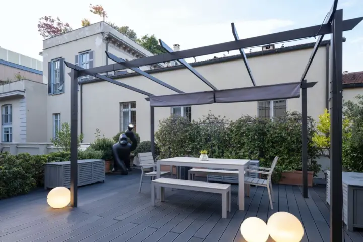 Terrazze arredate con tavolo, panche, sedie e scultura di gorilla sotto una pergola. Illuminazione soffusa con sfere luminose.