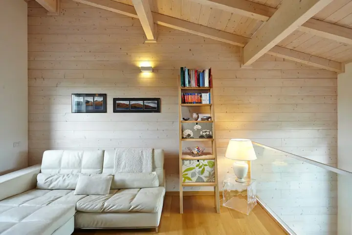Soggiorno accogliente con divano bianco, libreria a giorno e un suggestivo tetto in legno a vista.