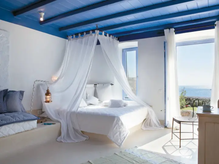 Camera da letto stile mediterraneo con soffitto blu, letto a baldacchino bianco e vista mare.
