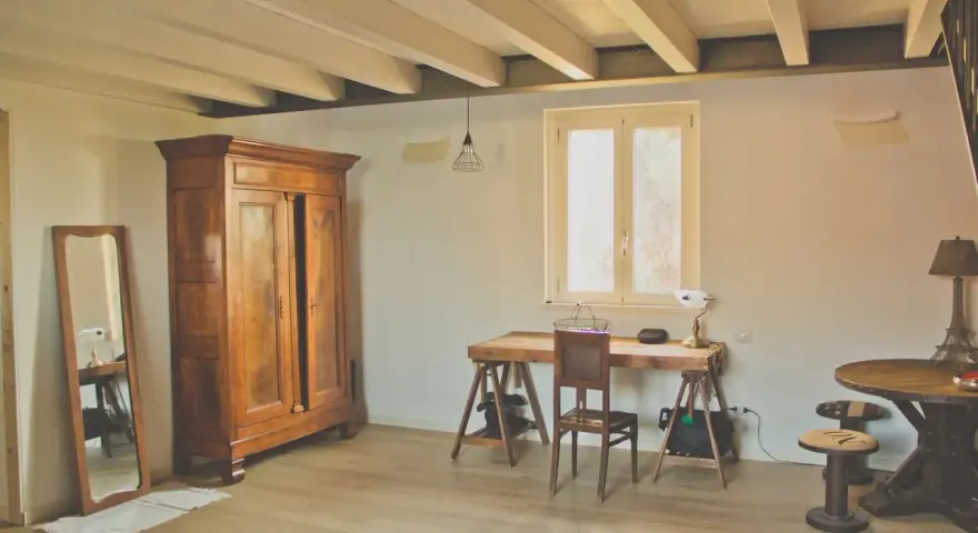 Arredamento casa di campagna: armadio antico in legno, specchio, scrivania rustica con sedia, tavolino rotondo e lampada a forma di Torre Eiffel.